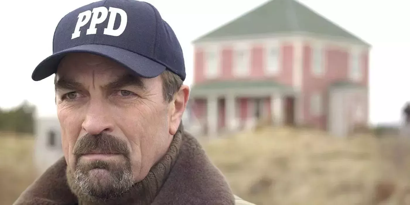 Jesse Stone (Tom Selleck) wearing a police department hat in front of a building in Stone Cold