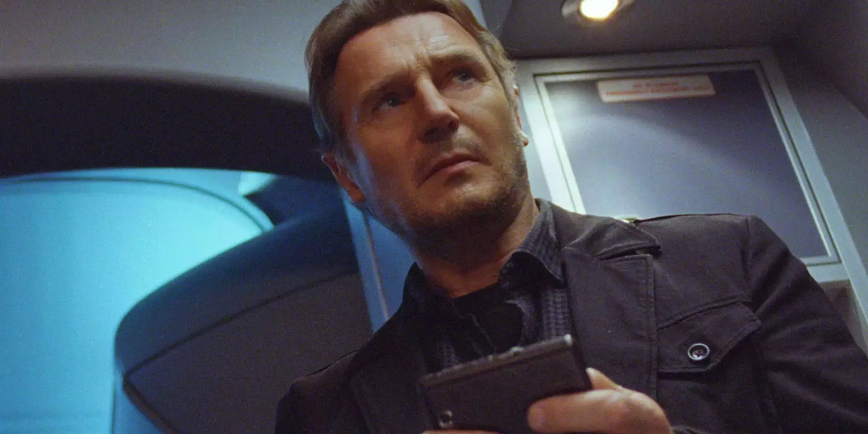 Bill Marks (Liam Neeson) looks in a wallet in an airplane bathroom in Non-Stop