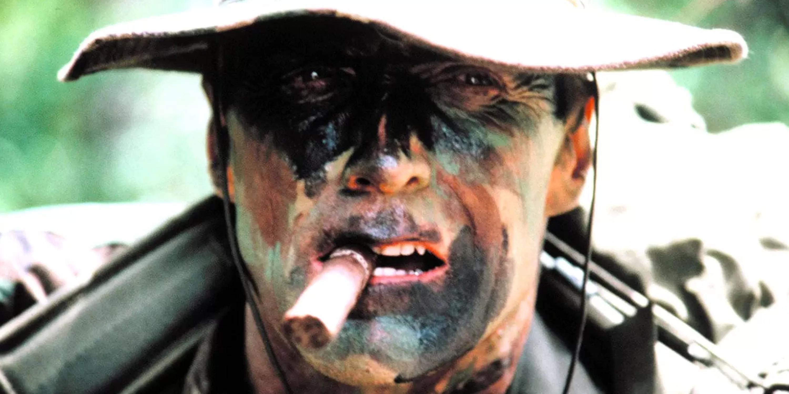 En un primer plano, Tom Highway fuma un cigarro con camuflaje pintado en su cara en Heartbreak Ridge.