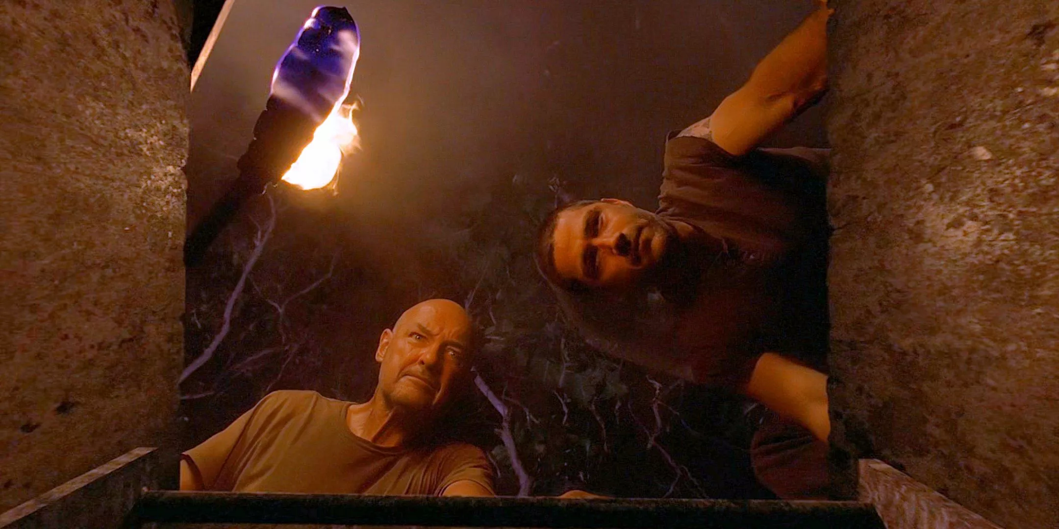 John Locke holds a torch with Jack Shephard next to him as they both peer down into the opened hatch in Lost