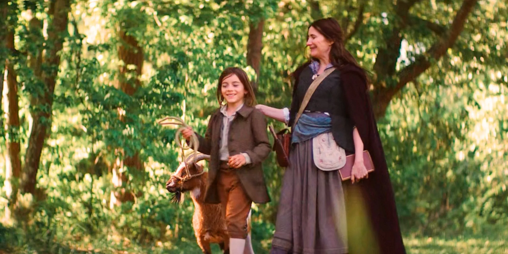 Agatha Harkness and Nicholas Scratch walk a goat down a path as they smile and laugh together from Agatha All Along