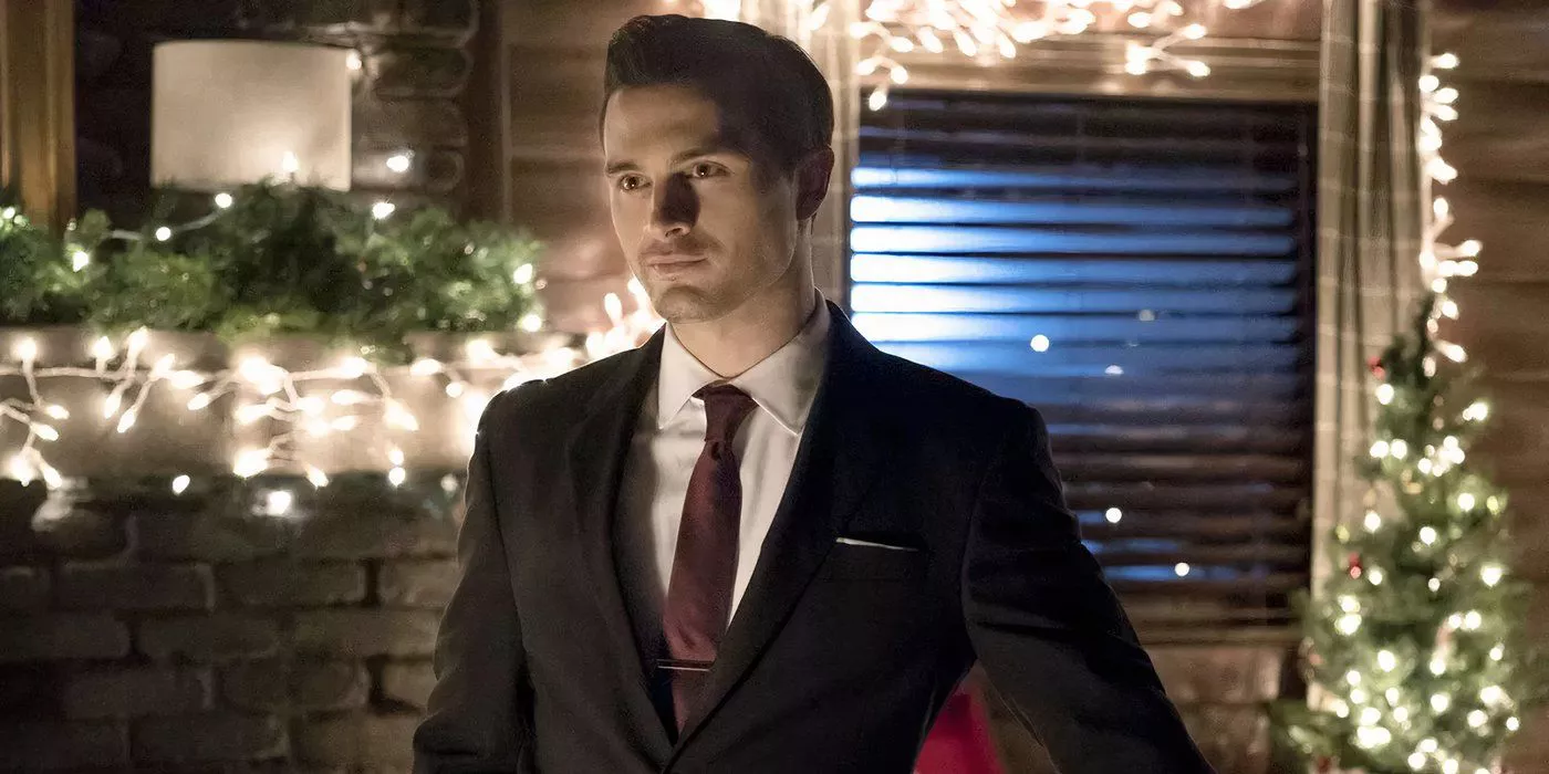 Michael Malarkey as Enzo stands at a doorway in a suit in The Vampire Diaries.