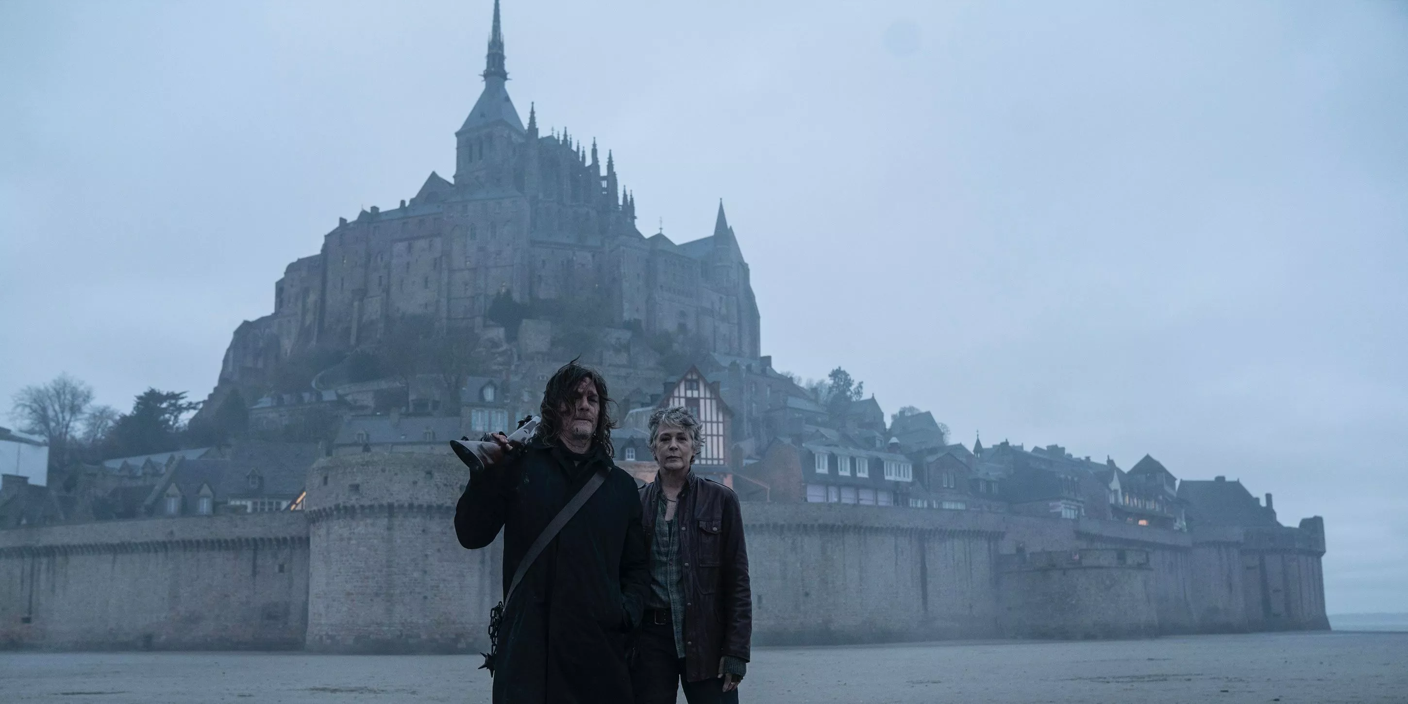 Daryl Dixon y Carol Peletier de pie frente al Mont-Saint-Michel en The Walking Dead: Daryl Dixon