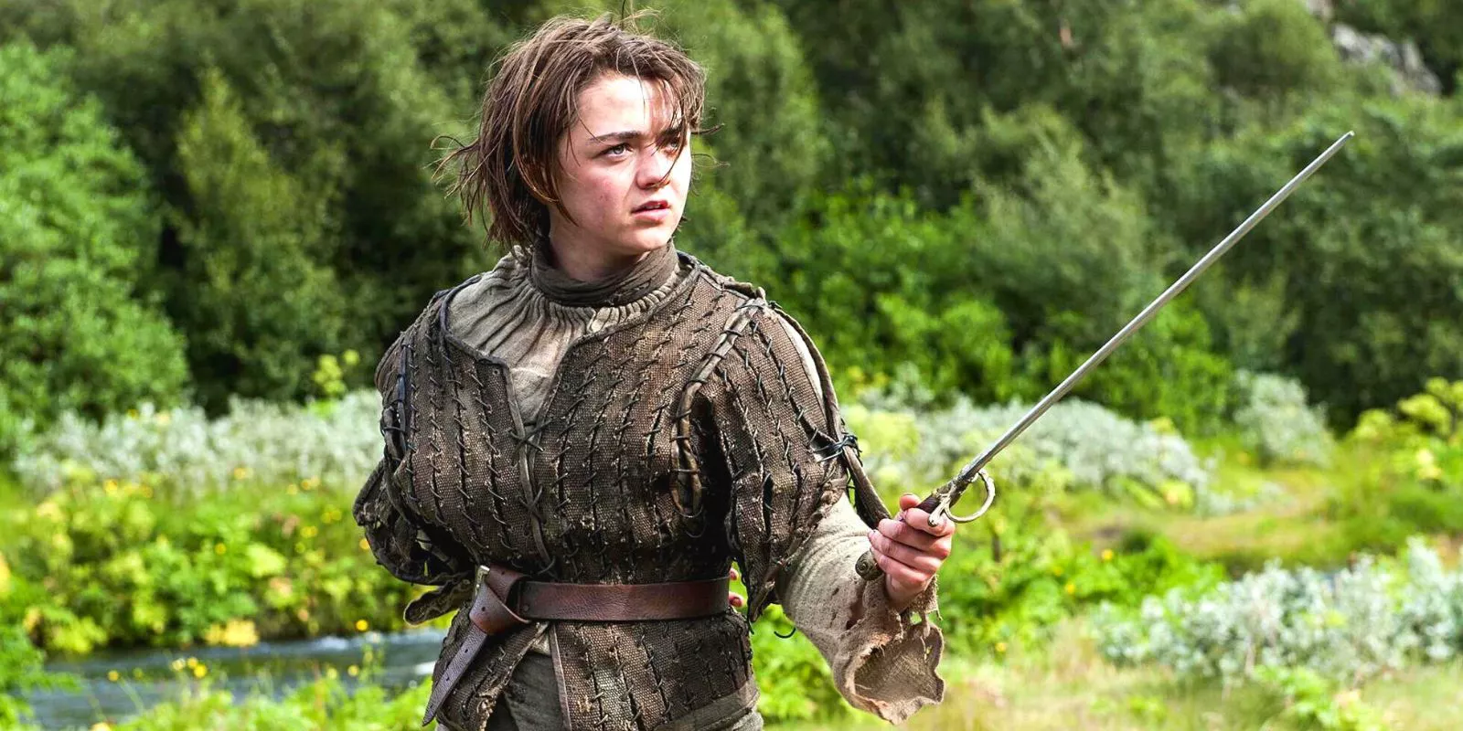 Arya Stark (Maisie Williams) sosteniendo su espada lista en un campo verde en Game of Thrones.