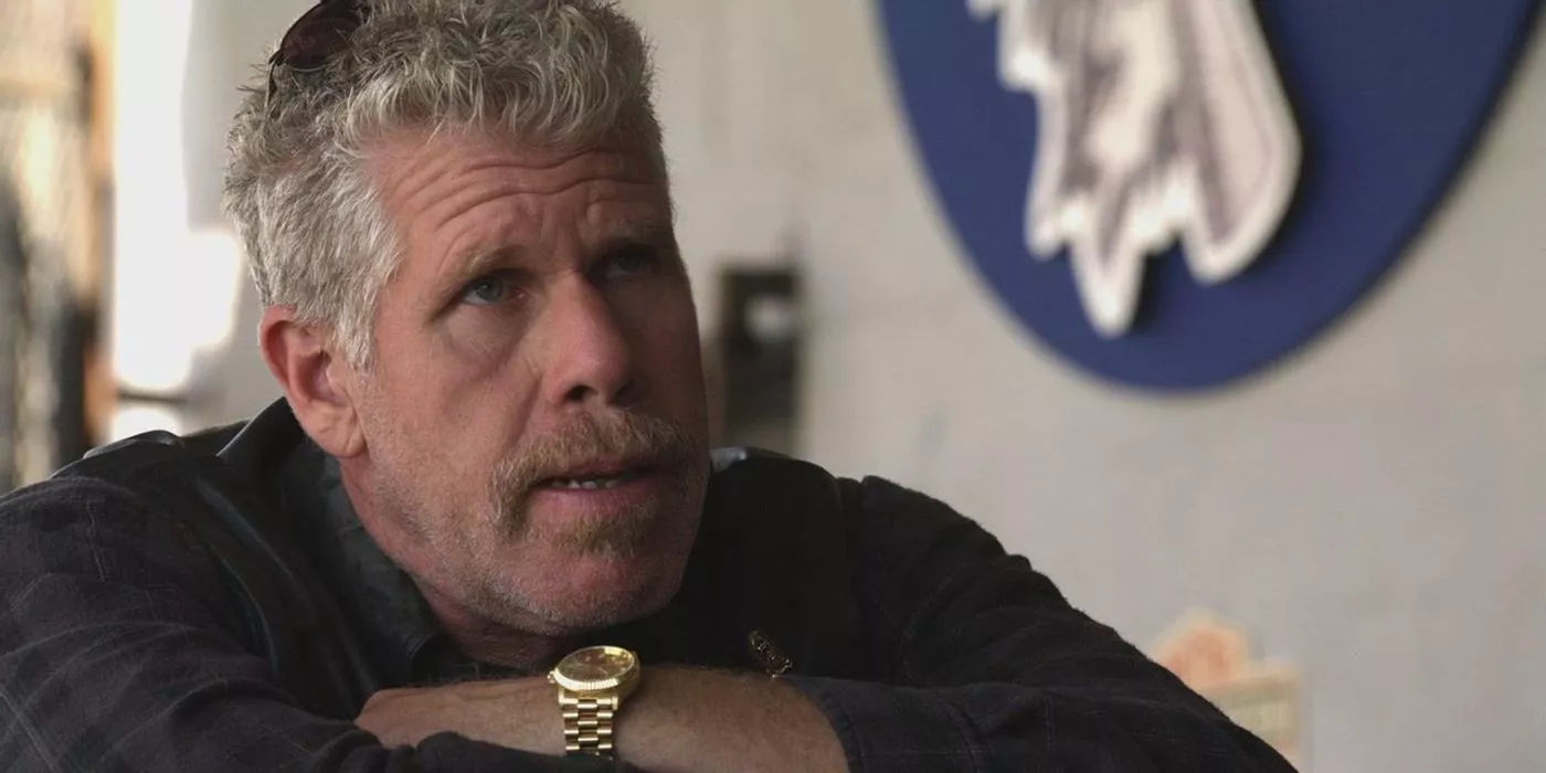 Clay Morrow sentado en una mesa con los brazos cruzados